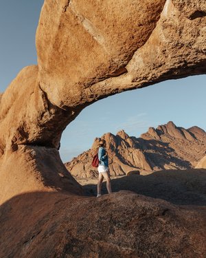 Frau steht unter einer riesigen, natürlichen Felsbrücke