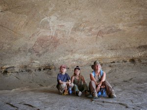 Mutter mit zwei Kindern sitzt unter einem Felsen mit Malereien