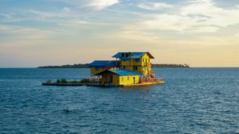 Eine Insel aus drei gelben Häusern mitten im Meer im Sonnenuntergang