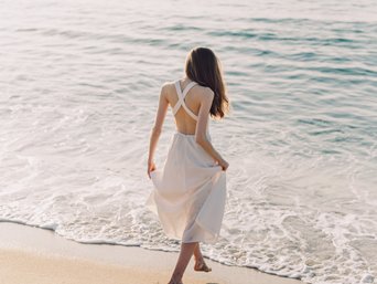 Frau in weißem Kleid läuft am Strand