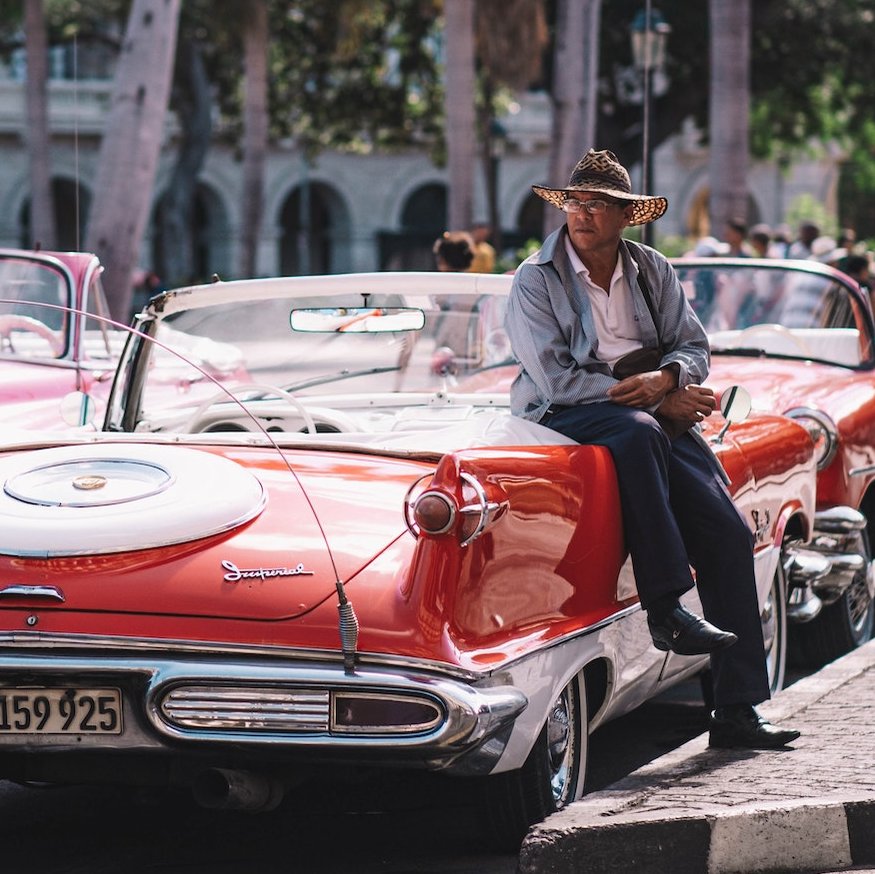 Mann mit Hut ist an Oldtimer gelehnt