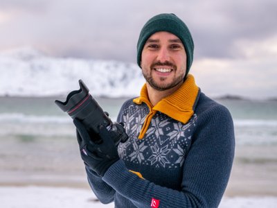 Fotograf Julien Pröpper mit Kamera in der Hand vor dem Meer