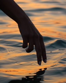 Hand nahe am Meerwasser bei Sonnenuntergang