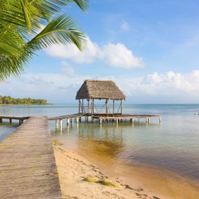 Ein Steg führt an einem Sandstrand ins Wasser zu einem Stelzenhaus