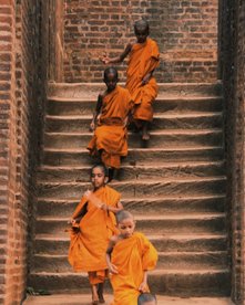 Kinder in orangener Robe der Mönche laufen eine steinerne Treppe hinunter