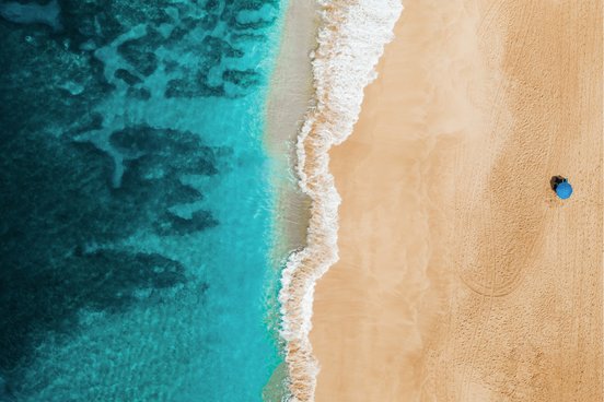 Mensch mit Sonnenschirm liegt am Strand