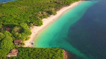 Luftansicht einer Landzunge mit feinem Sandstrand, üppigem Grün und türkisblauem Wasser