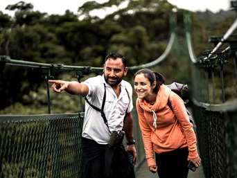 Reiseleiter Alvaro Jimenez zeigt einer Frau etwas während sie auf einer Hängebrücke stehen