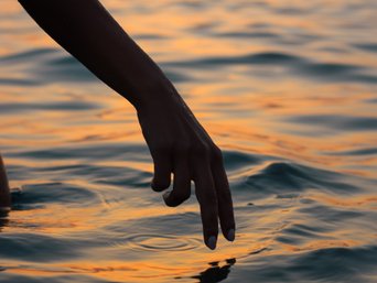 Hand nahe am Meerwasser bei Sonnenuntergang