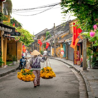 Verkäufer mit 2 Stohkörben lauft durch bunte Straße