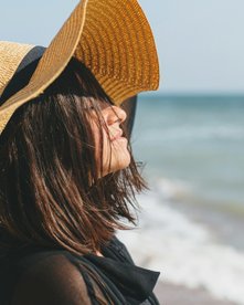 Frau mit Hut von der Seite am Strand