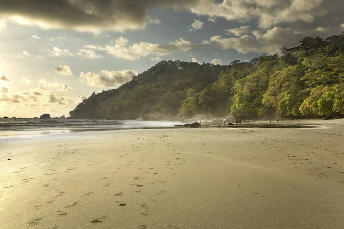 Sonnenuntergang am Sandsrand mit grünen Bergen im Hintergrund