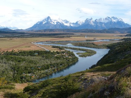 Patagonien Rundreise Selbstfahrer - Torres del Paine - Fluss mäandert durch grüne Ebene mit Bergen im Hintergrund unter bewölktem Himmel