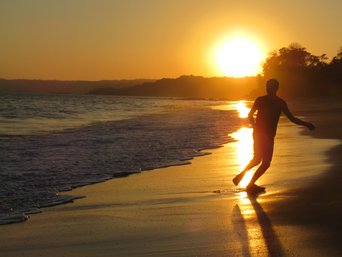 Mensch rennt im Sonnenuntergang am Strand entlang im Gegenlicht
