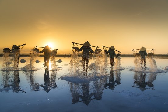 Menschen mit Hüten und Netzten im Wasser bei Sonnenuntergang