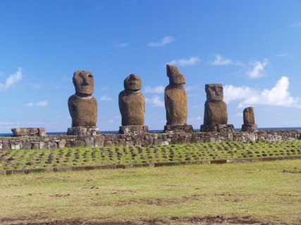 Osterinsel - Fünf große Moai-Skulpturen auf einer steinernen Plattform vor blauem Himmel und grünem Gras