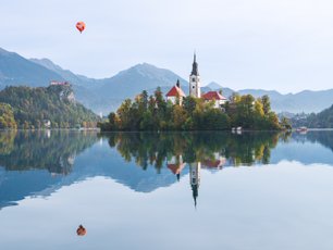 Kirche auf einer kleinen Insel spiegelt sich im See mit Bergen im Hintergrund