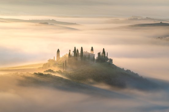 Nebeliger Hügel in der Toskana auf dem eine Villa steht mit Zypressen