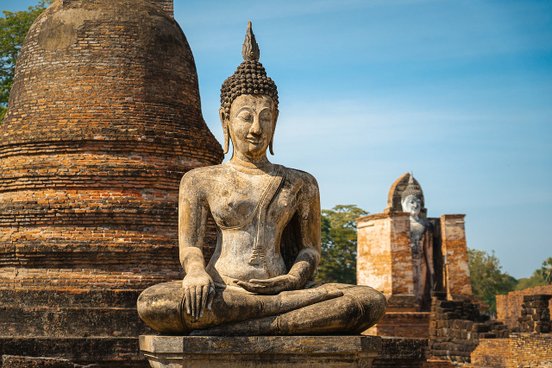 Sitzende Buddha Statue aus hellbraunem Stein vor Pagode