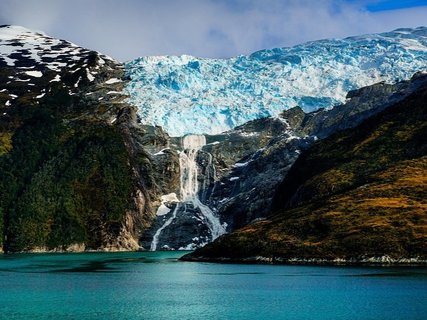 Patagonien Rundreise Selbstfahrer - Romanche Gletscher Beagle Kanal - Gletscher mit Wasserfall zwischen bewaldeten und felsigen Bergen über einem türkisfarbenen See