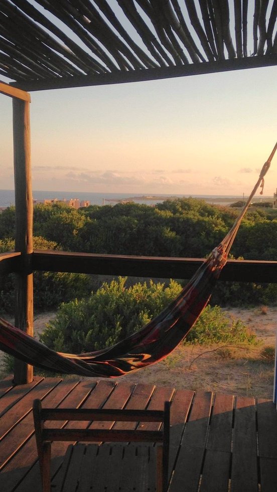 Hängematte auf Holzterrasse mit Blick auf grüne Büsche und Küste im Sonnenuntergang