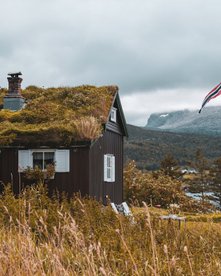 Ein braunes Holzhaus im typischen Stil am See mit norwegischer Flagge