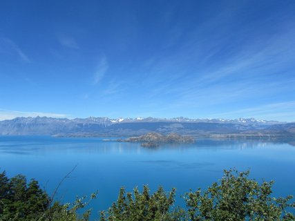 Patagonien Rundreise Selbstfahrer - Lago General Carrera - Blick über einen großen See mit Inseln und bewaldetem Ufer im Vordergrund vor einer Bergkette unter blauem Himmel
