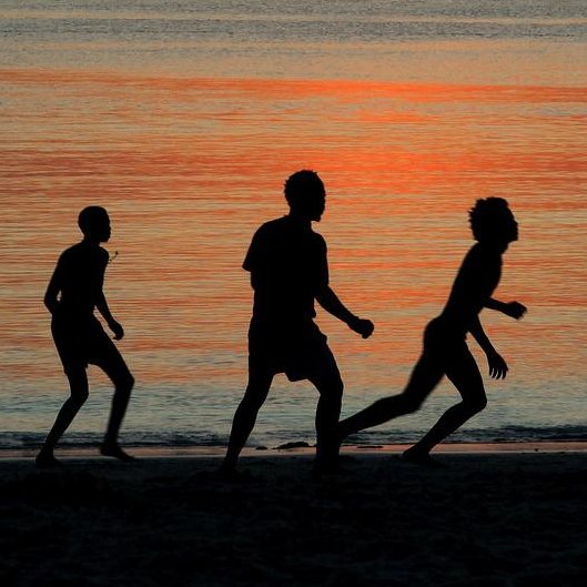Fußballspielende Männer im Schatten der Abendsonne am Strand.