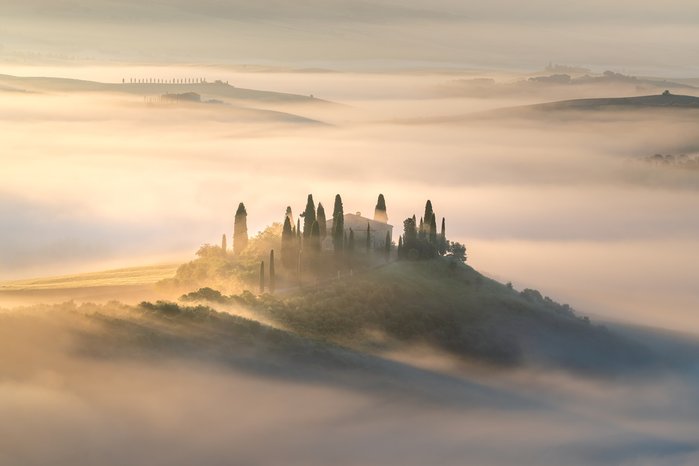 Nebeliger Hügel in der Toskana auf dem eine Villa steht mit Zypressen