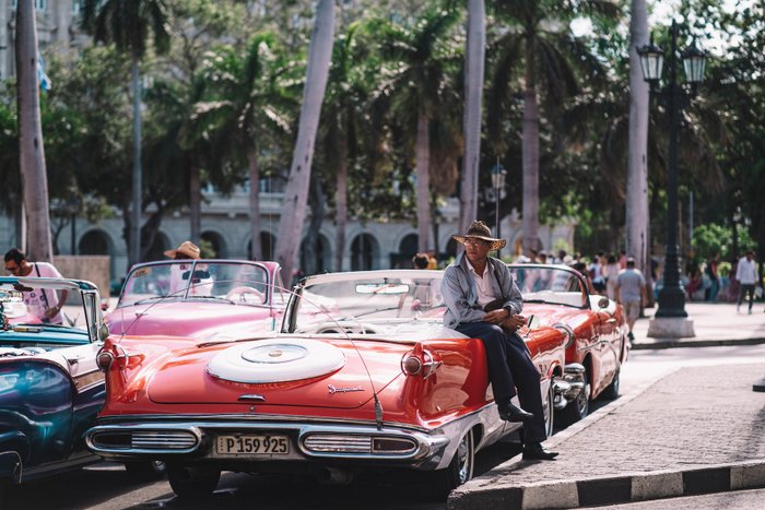 Mann mit Hut ist an Oldtimer gelehnt