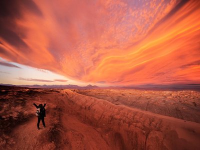 Fantastischer Sonnenuntergang in rot und orange in der Atacamawüste. Ein Mensch am unteren Rand im Bild bestaunt die Natur. 