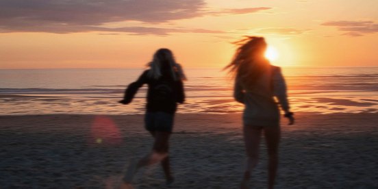 Zwei Frauen rennen am Strand entlang bei Sonnenuntergang