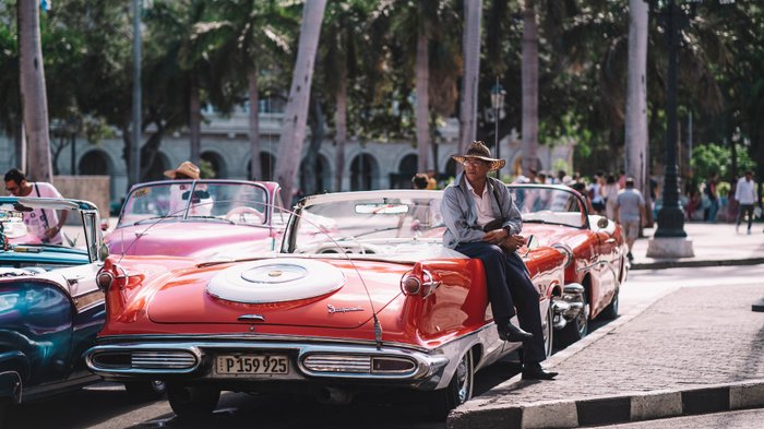 Mann mit Hut ist an Oldtimer gelehnt