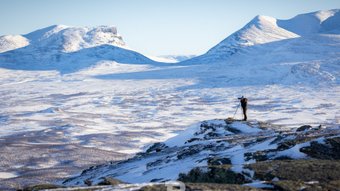 Fotograf mit Stativ in einer schneebedeckten weiten Berglandschaft
