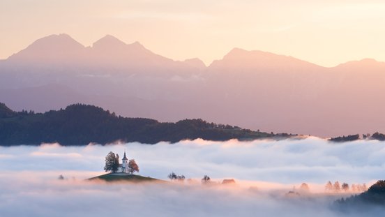 bergige Landschaft mit Kirche über Nebel zu Sonnenuntergang
