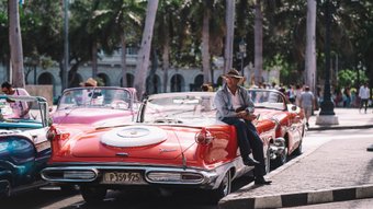 Mann mit Hut ist an Oldtimer gelehnt