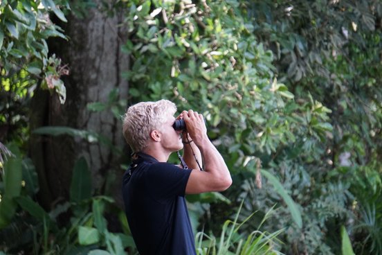 Blonder Mann schaut durch ein Fernglas und beobachtet Vögel
