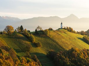 Kirche auf grünem Hügel im Morgenlicht mit Bergen im Hintergrund
