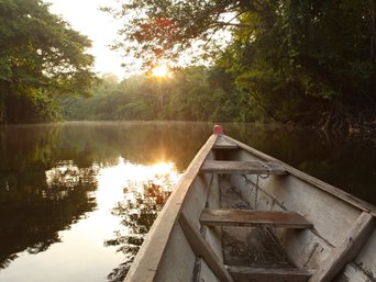 Blick von einem Holzboot aus auf den Sonnenuntergang über dem Fluss