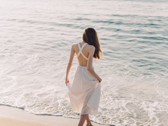Frau in weißem Kleid läuft am Strand