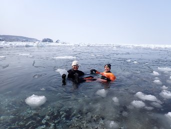 Zwei Menschen schwimmen im Trockenanzug im Eismeer