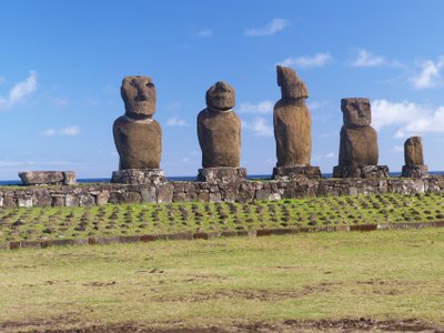 Osterinsel - Fünf große Moai-Skulpturen auf einer steinernen Plattform vor blauem Himmel und grünem Gras