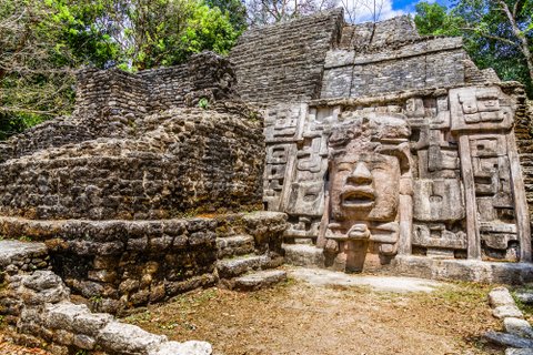 Old ancient stone Mayan pre-columbian civilization pyramid with carved face and ornament hidden in the forest, Lamanai archeological site, Orange Walk District, Belize