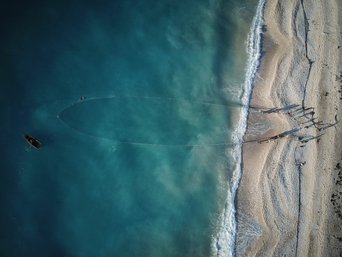 Ein Strand von oben, außerdem Menschen und ein Fischernetz
