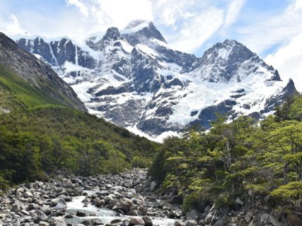 Patagonien Rundreise Selbstfahrer - Torres del Paine - Berglandschaft mit schneebedeckten Gipfeln, bewaldeten Hängen und einem felsigen Fluss im Vordergrund