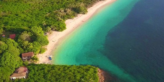 Luftansicht einer Landzunge mit feinem Sandstrand, üppigem Grün und türkisblauem Wasser