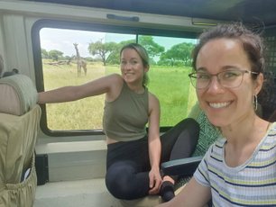 Zwei Menschen im Jeep und Giraffe im Hintergrund