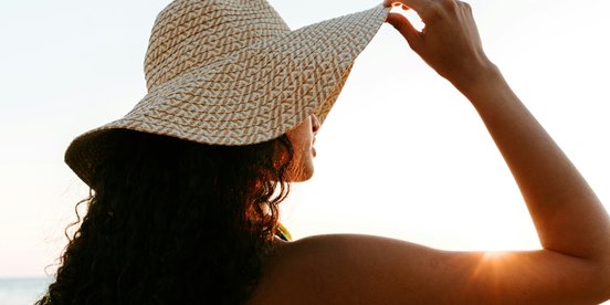 Frau mit einem großen Sonnenhut schaut in den Sonnenuntergang