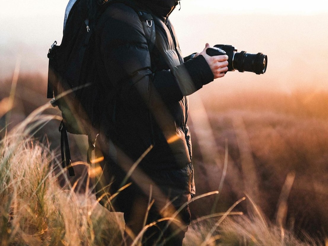Mann hält Kamera in der Hand. Im Hintergrund ein schöner Sonnenuntergang