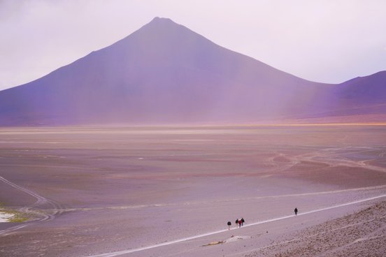 Menschen wandern in karger Landschaft mit Vulkan im Hintergrund